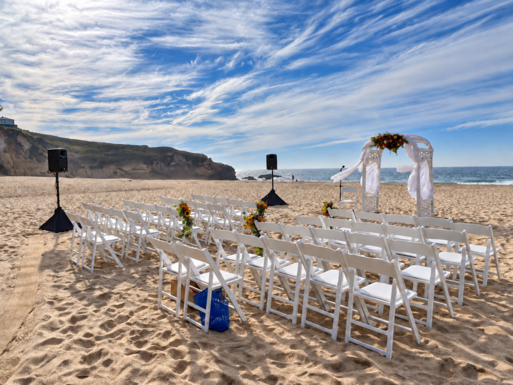 Battery-operated speakers beside white chairs and a wedding arch at a Bay Area beach ceremony