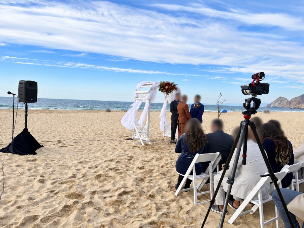 Beach wedding ceremony with sound system, couple and guests, with faces blurred for privacy